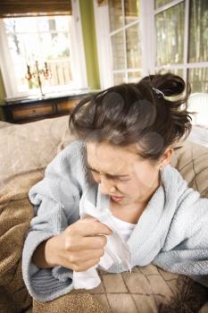 Young ill woman in bathrobe sneezes into a tissue. Vertical shot.