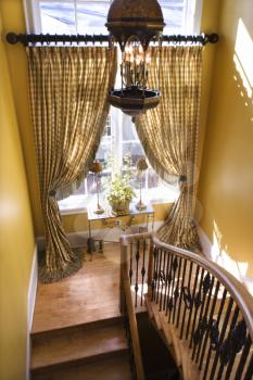 High angle view of stair landing with curtained window and ornate banister. Vertical shot.
