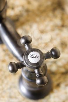 Selective focus close-up of stainless steel cold water faucet handle on marble counter top. Vertical shot.