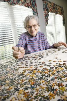 Smiling elderly woman putting together a jigsaw puzzle. Vertical shot.