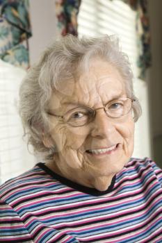 Elderly woman in glasses smiles towards the camera.  Vertical shot.