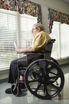 Elderly man reads a newspaper while sitting in wheelchair. Vertical shot.