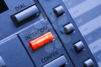 Close up of a multi-line business telephone with a lit intercom button. Horizontal shot.