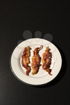 Three strips of cooked bacon on a white plate. Vertical shot.