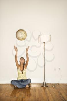 Attractive young woman smiling and sitting on the floor next to a floor lamp. She is tossing a globe into the air. Vertical shot.