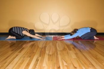 Two women kneel towards each other in child's pose yoga position at the gym. Horizontal shot.