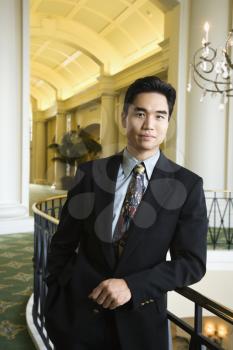 Portrait of an Asian business man leaning on a rail in an upscale hotel. Vertical shot.