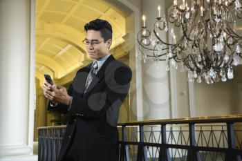 A young Asian businessman types on his mobile phone in an upscale hotel. Horizontal shot.