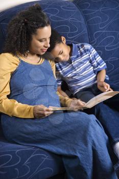 A mid adult woman sitting on a couch reading a book to her young son. Vertical shot.