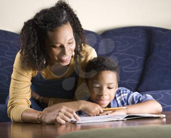 A mid adult African American woman sits on a couch while helping her young some with his homework. Horizontal shot.