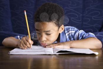 Young African American boy sitting on the floor in front of a coffee table doing homework. Horizontal shot.