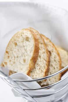 Sliced white bread sitting in a stainless steel bread basket lined with linen. Vertical shot.