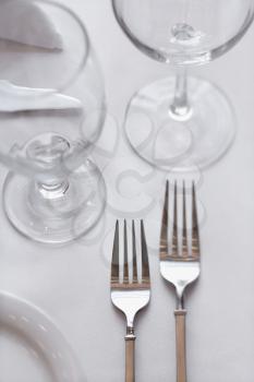 Two forks sitting on a dining table with a white tablecloth. Vertical shot.