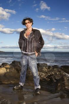 A young man dressed in casual clothing poses at the beach. Vertical shot.