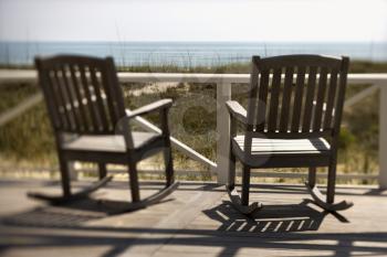 Two wooden rocking chairs sitting on a deck. They are facing the shore. Horizontal shot.