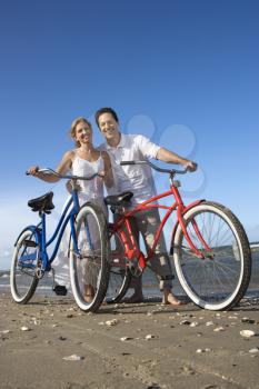 Smiling man and woman pose with bicycles on the sand near the beach. Vertical shot.