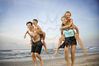 Mother and father give their children piggy back rides at the beach. Horizontal shot.