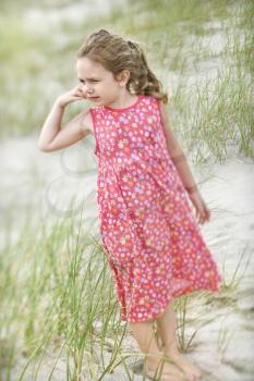 Little girl in a dress stands barefoot on the beach. Vertical shot.