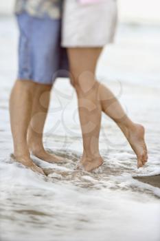 Waist down image of affectionate couple standing in the water at the beach. Vertical shot.
