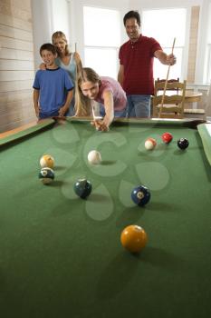 Girl playing pool with family in background. Vertically framed shot.