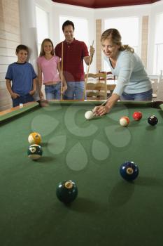 Woman playing pool with family in background. Vertically framed shot.