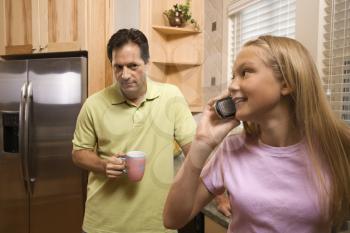 Father watching daughter talk on cell phone while in kitchen