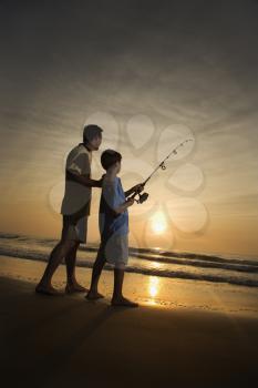 Father and son fishing in ocean surf at sunset.  Vertically framed shot.