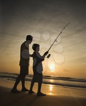 Father and son fishing in ocean surf at sunset.  Vertically framed shot.