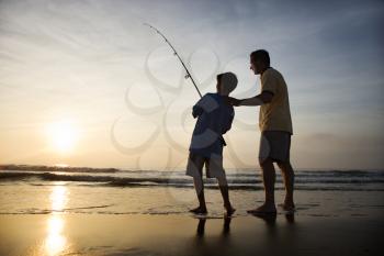 Father and son fishing in ocean surf at sunset. 