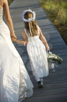 Cropped rear view of a bride walking and holding hands with a flower girl on the boardwalk. Vertical shot.