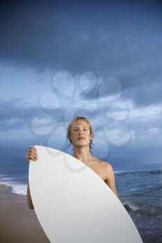 Young male surfer standing on beach with surfboard. Vertical shot