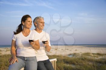 Couple sitting and relaxing together at the beach with glasses of red wine. Horizontal shot