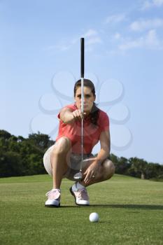 Woman crouches and lines up her putt on a golf course. Vertical shot.