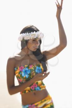 Attractive young Hawaiian woman in tropical flower print summer attire and a lei on her head dancing with hands in hula position. 