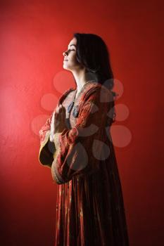 Attractive young woman standing against a red wall with hands held in prayer and eyes closed. Vertical shot. Isolated on red. 