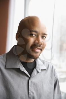 Head and shoulders portrait of an attractive African-American man smiling near a window. Vertical shot.
