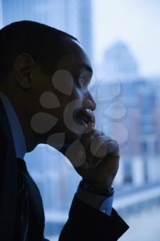 Close-up profile of an African-American mid-adult businessman with hand on chin in front of window. Vertical format.