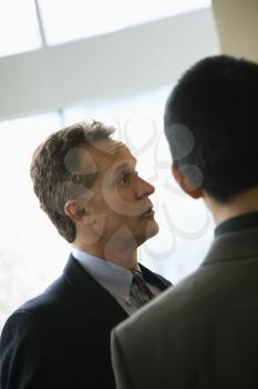 Cropped view of a Caucasian middle-aged businessman and a young adult businessman in a discussion. Vertical format.
