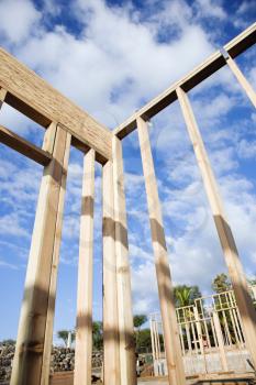 Section of a construction wall framed out in wood against a blue sky. Another framed building can be seen in the background. Vertical shot.
