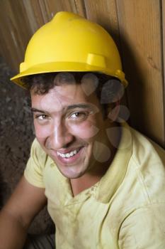 Portrait of a Caucasian male construction worker in a yellow hardhat as he rests against a fence and smiles towards the camera. Vertical shot.