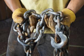 Close up of a Caucasian male construction worker holding a hook and chains in his gloved hands. Horizontal shot.
