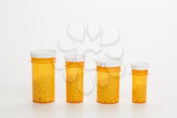 Yellow medicine bottles with pills in diminishing sizes lined up in a row. Horizontal shot. Isolated on white.