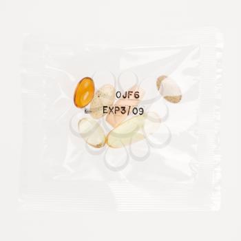 Pack of daily vitamin supplements in a clear plastic bag, stamped with an expiration date. Square format. Isolated on white.