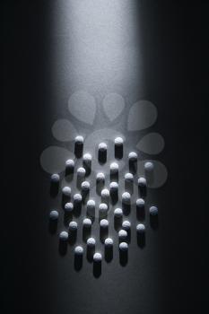 Overview of white round pills on a dark background, arranged in a circle. They are illuminated in a shaft of light. Vertical shot.