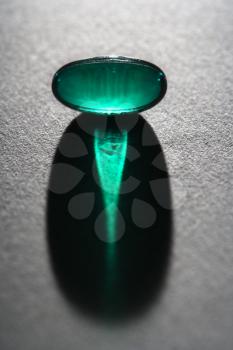 Close up of a translucent green capsule backlit and casting shadow. Vertical shot.