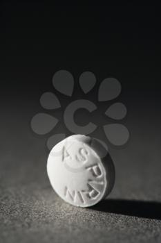 Close up of a round white aspirin standing on side on a gray background casting a shadow.