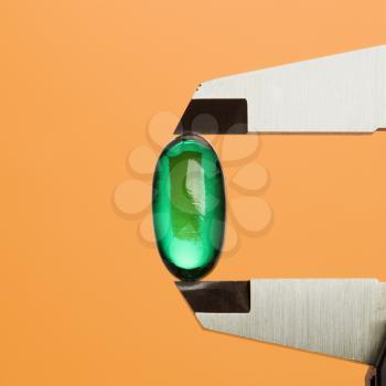 Green capsule pill in a caliper. Square format. Isolated on orange.