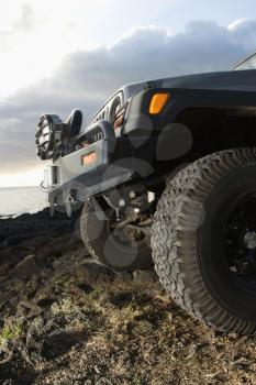 Low angle close-up of front of SUV on a rocky beach. Vertical format.