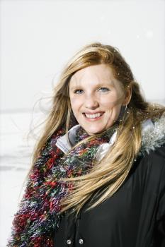 Young woman facing the camera and wearing a coat and scarf in winter conditions. Vertical shot.
