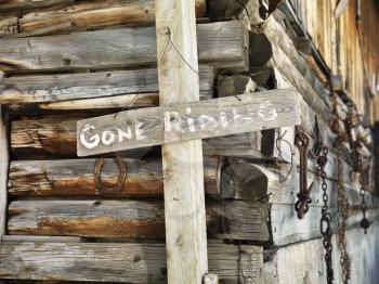 'GONE RIDING' sign against an old weathered, wooden stable. Horizontal shot.